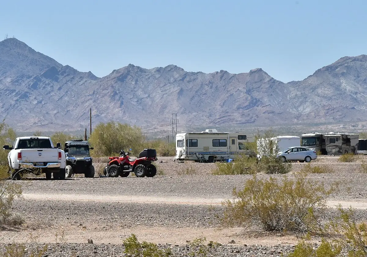 RVs and trucks parked on open desert ground with rocky mountains behind