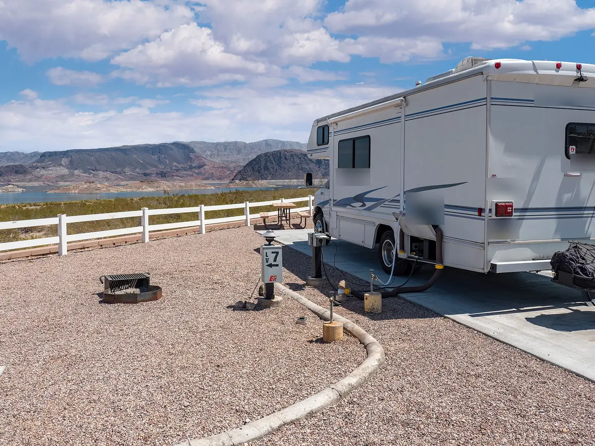 Class C motorhome hooked up to water and power at a gravel RV site above a desert lake