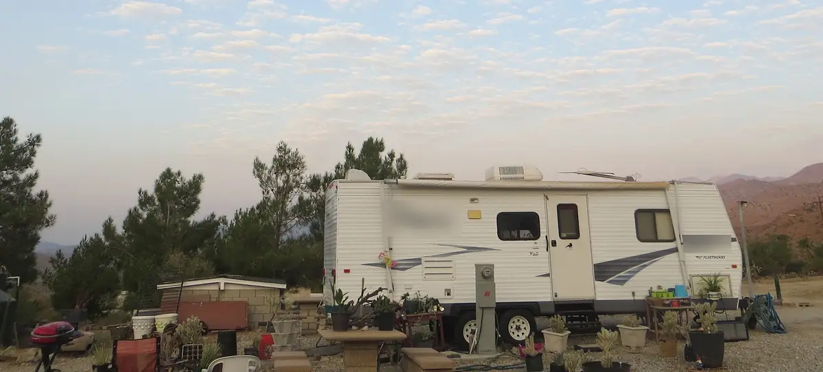 Travel trailer with a rooftop AC unit parked at a high desert lot at dusk